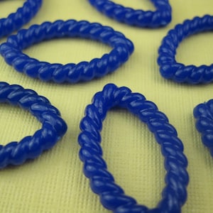 May include: Several oval-shaped, deep blue rings with a twisted rope design. The rings are scattered across a light yellow surface, with some overlapping. The glossy finish of the rings reflects the light, highlighting their texture and shape.