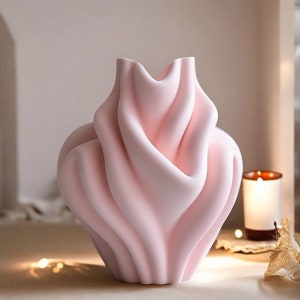 May include: A pink ceramic vase with a unique, organic, and flowing design. The vase is shaped like a series of soft, rounded folds, creating a visually interesting and modern aesthetic.
