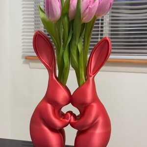 Puede incluir: Dos jarrones de cer&aacute;mica de conejo rojo que se miran, sosteniendo un ramo de tulipanes rosas.