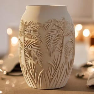 Könnte beinhalten: Eine weiße Keramikvase mit einem geprägten Design aus Palmen und Blättern.