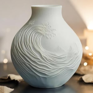 May include: A white ceramic vase with a detailed, embossed design of a wave crashing. The vase has a light blue glaze at the bottom.