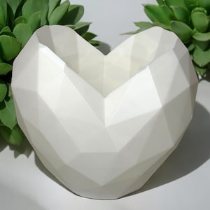 May include: White ceramic heart-shaped planter with a geometric design. The planter is made of a smooth, matte finish ceramic and has a wide opening at the top.