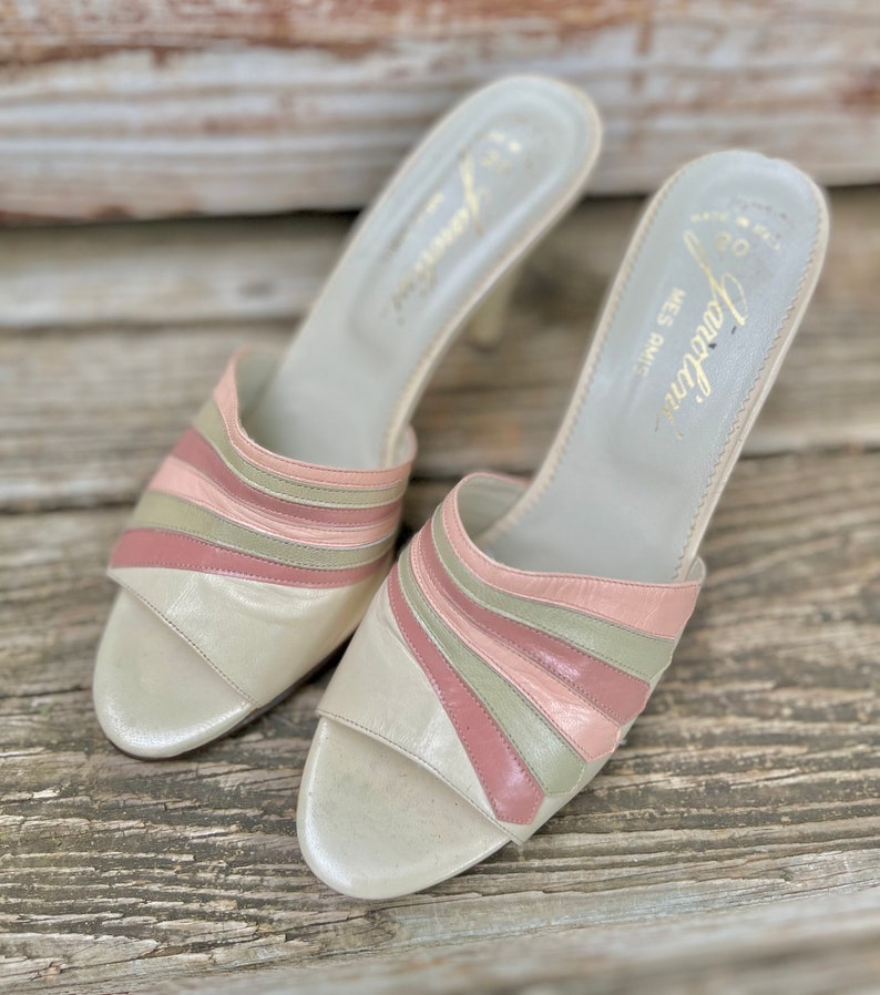 May include: A pair of white leather heeled sandals with pink and green striped detailing. The sandals are open-toed and have a low heel. The brand name "Fontana" is printed on the insole.
