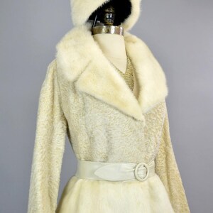 May include: A white fur coat with a matching fur hat and a white leather belt with a silver buckle.