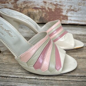 May include: A pair of white leather heeled sandals with pink and green striped detailing. The sandals are made by the brand "Modolini" and have a high heel.