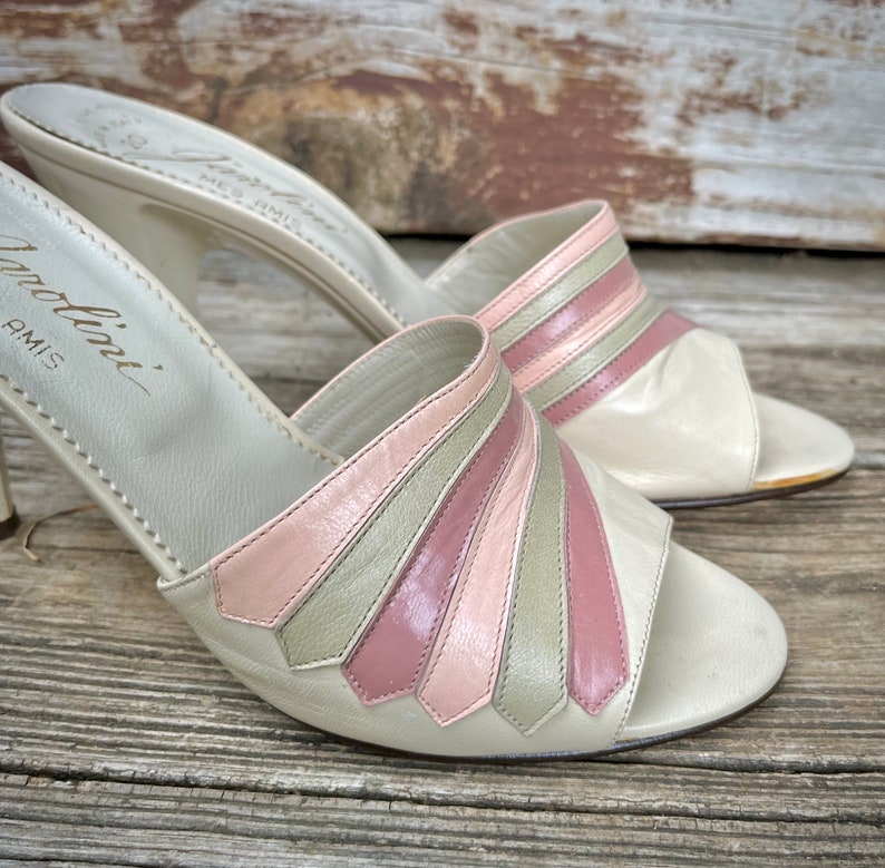 May include: A pair of white leather heeled sandals with pink and green striped detailing. The sandals are made by the brand "Modolini" and have a high heel.