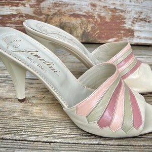 May include: A pair of white leather heeled sandals with pink and green striped detailing. The sandals are labeled "Gianolini Mes Amis" on the insole.