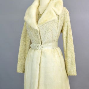 May include: A white fur coat with a large fur collar and a white satin belt. The coat is on a mannequin.