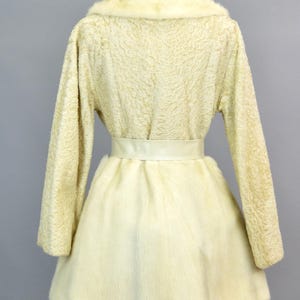 May include: A white faux fur coat with a white satin belt. The coat has a collar and long sleeves.