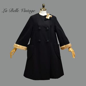 May include: A vintage black coat with a double-breasted design, featuring a round collar and fur trim on the cuffs. The coat has two front pockets and is displayed on a mannequin. The text "La Belle Vintage" is visible.