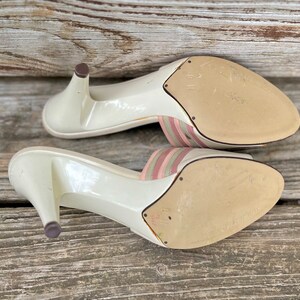 May include: A pair of white heeled sandals with pink and green striped straps. The sandals have a pointed toe and a high heel.