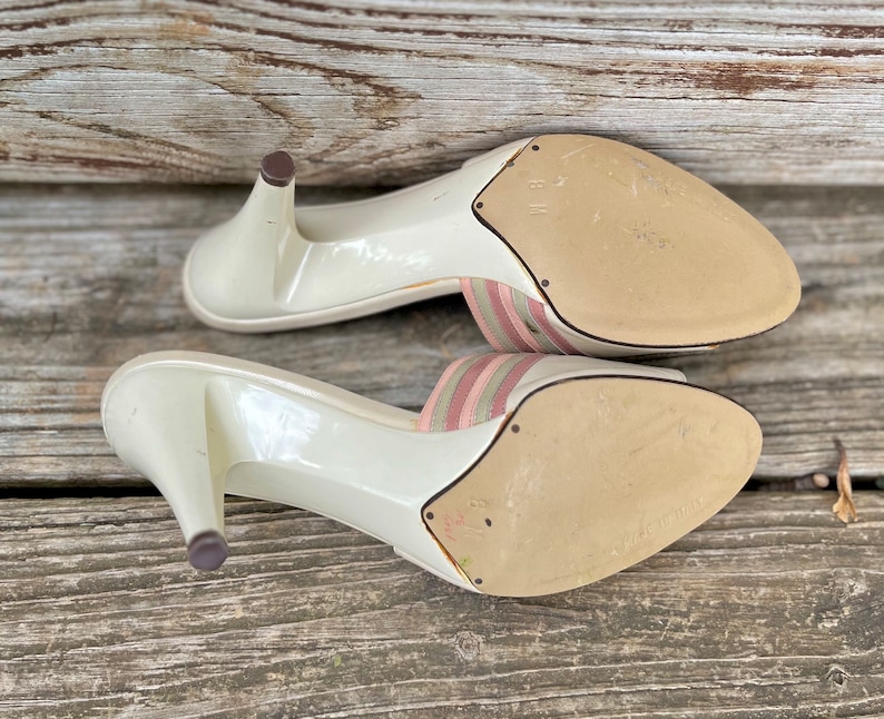 May include: A pair of white heeled sandals with pink and green striped straps. The sandals have a pointed toe and a high heel.
