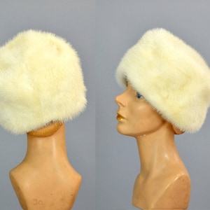 May include: A white fur hat with a wide brim. The hat is made of soft, fluffy fur and has a simple, elegant design.