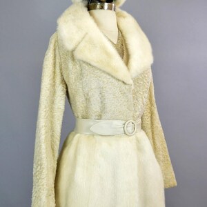 May include: A white fur coat with a matching fur hat and a white leather belt. The coat has a long, flowing style and a large collar.