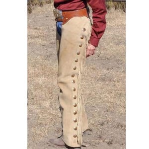 May include: A pair of tan leather chaps with fringe and a row of brass buttons down the side.