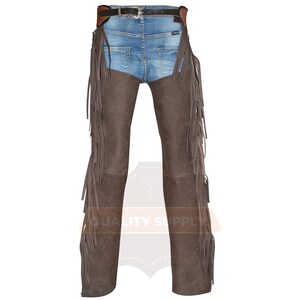 May include: Brown leather chaps with long fringe detailing. The chaps are worn over blue denim jeans, with a brown leather belt and silver buckle. The chaps have a suede-like texture and are designed for riding or Western wear.