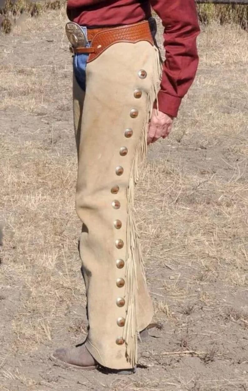 May include: A pair of tan leather chaps with fringe and a row of silver buttons down the side.