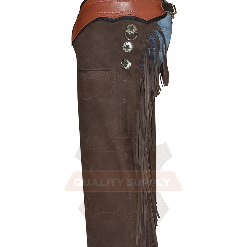 May include: Brown leather chaps with a brown leather belt and fringe detailing. The chaps have silver-coloured decorative buttons and a pocket. The top portion is a lighter brown colour.