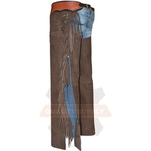 May include: Brown leather chaps with fringe and a zip. The chaps have decorative metal buttons and a brown leather belt. The top section is a lighter brown. The chaps are worn over blue jeans.