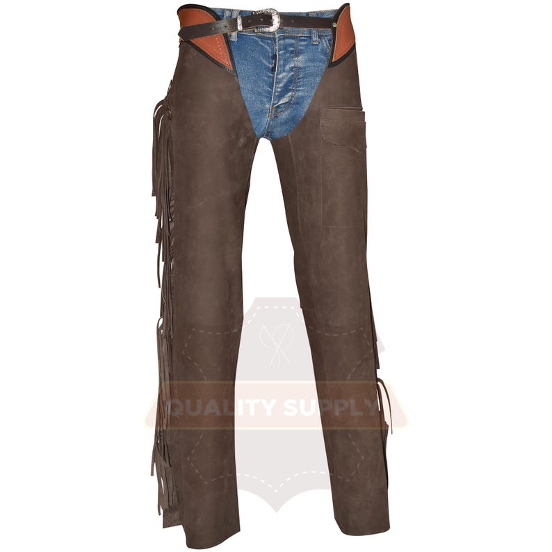May include: Brown leather chaps with fringe detailing along the outer seams. The chaps are worn over blue denim jeans and a brown and black belt with a silver buckle. A pocket is visible on the right leg.