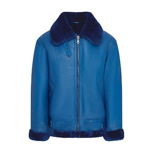 Puede incluir: Chaqueta de cuero azul brillante con cuello y puños de borrego azul oscuro. La chaqueta presenta una cremallera frontal, un detalle de hebilla en el cuello y un estilo aviador clásico.