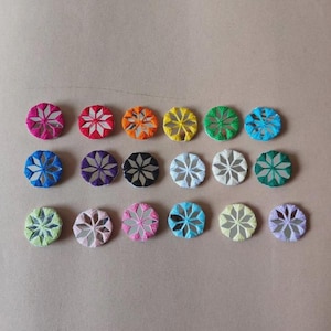 May include: A collection of twenty colorful, circular embroidered patches. Each patch features a mirrored center and a starburst design, with colors including pink, red, orange, yellow, green, and blue. The patches are arranged on a neutral background.