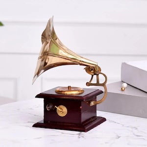 May include: A vintage-style gramophone with a polished brass horn and a dark wood base. The gramophone features a gold-colored turntable and a hand crank. This decorative piece evokes a classic, antique aesthetic.