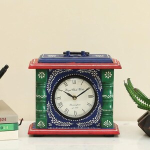 Puede incluir: Un reloj rectangular pintado a mano con esfera azul y diseño floral blanco. El reloj tiene base y parte superior rojas, pilares verdes y el texto "Royal Clock Works Birmingham est. 1792".