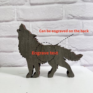 May include: A wooden wolf silhouette with a grey woodgrain finish. The wolf is howling and has a space on the back for engraving text. "Can be engraved on the back" and "Engrave text" are written on the image.