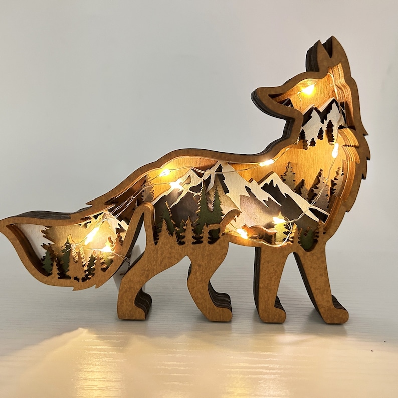 May include: A wooden fox silhouette with a layered mountain scene inside. The fox is standing on a white surface and has warm white LED lights inside.