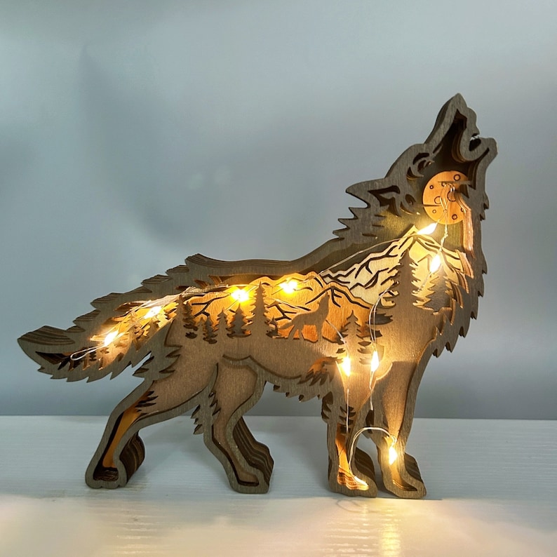 May include: A wooden wolf silhouette with a forest scene inside, illuminated by warm white fairy lights. The wolf is howling at the moon, and the forest scene includes trees, mountains, and a small wolf.