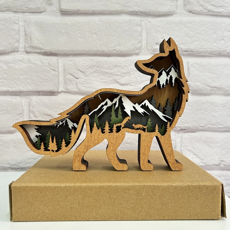 May include: Wooden fox silhouette with a mountain landscape scene inside. The fox is standing on a brown wooden base.