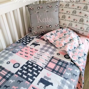 May include: A pink and gray patchwork toddler bedding set with a farm theme. The bedding features a tractor, cows, pigs, horses, and the text "Cluck Oink BAA Moo Cluck". The set includes a pillow with the name "Kate" embroidered on it.