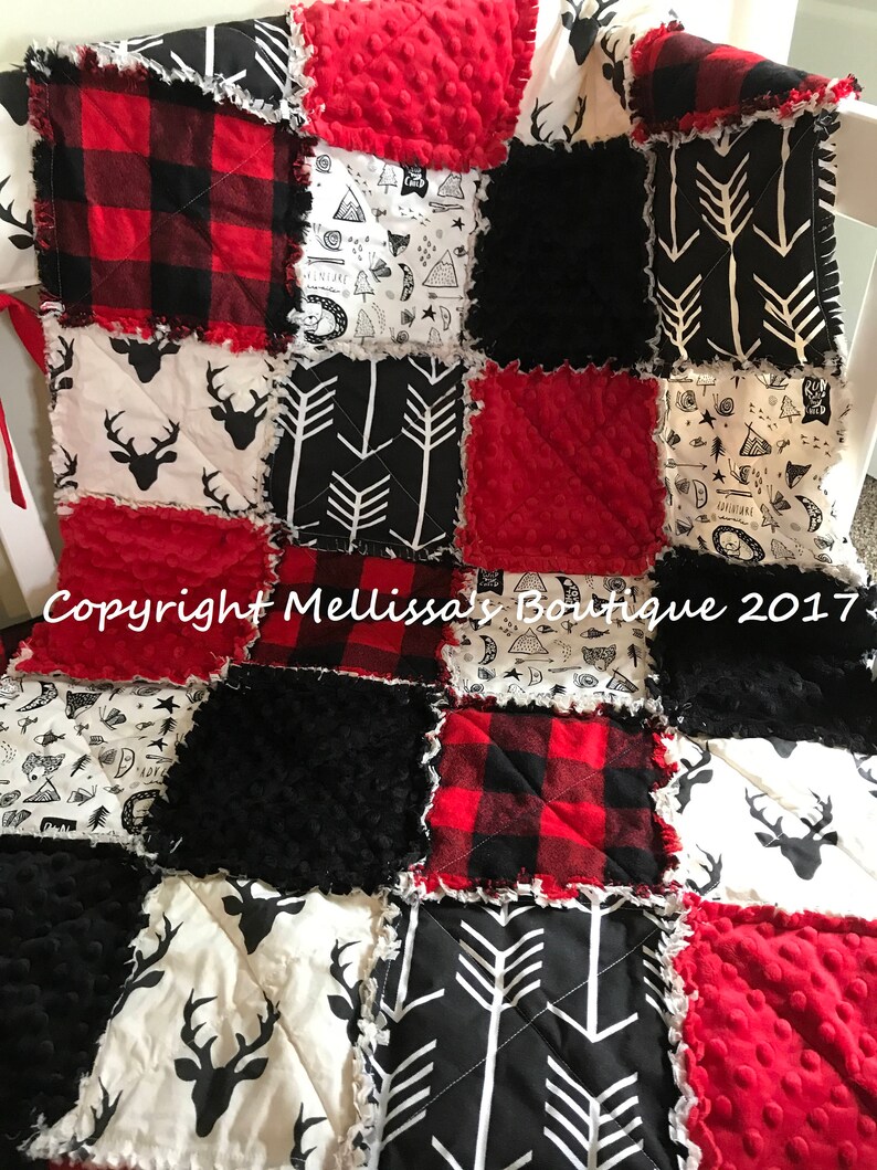 May include: A patchwork baby quilt with a woodland theme. The quilt features red and black buffalo plaid, black and white arrow patterns, and white fabric with black deer silhouettes. The quilt is made with a variety of textures, including minky fabric and flannel.