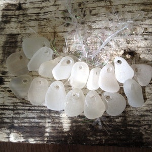 Puede incluir: Una colecci&oacute;n de piezas de vidrio de mar blanco con agujeros perforados. El vidrio de mar est&aacute; dispuesto en semic&iacute;rculo sobre una superficie de madera.