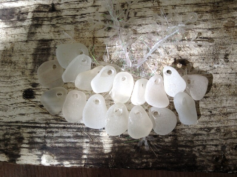 Puede incluir: Una colecci&oacute;n de piezas de vidrio de mar blanco con agujeros perforados. El vidrio de mar est&aacute; dispuesto en semic&iacute;rculo sobre una superficie de madera.