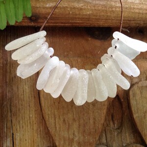 Puede incluir: Un collar hecho de cuentas de vidrio de mar blanco enhebradas en un alambre marr&oacute;n. Las cuentas son de varias formas y tama&ntilde;os, y todas son lisas y pulidas.