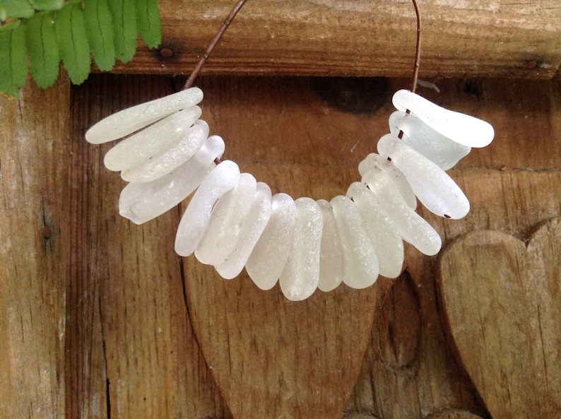 Puede incluir: Un collar hecho de cuentas de vidrio de mar blanco enhebradas en un alambre marr&oacute;n. Las cuentas son de varias formas y tama&ntilde;os, y todas son lisas y pulidas.