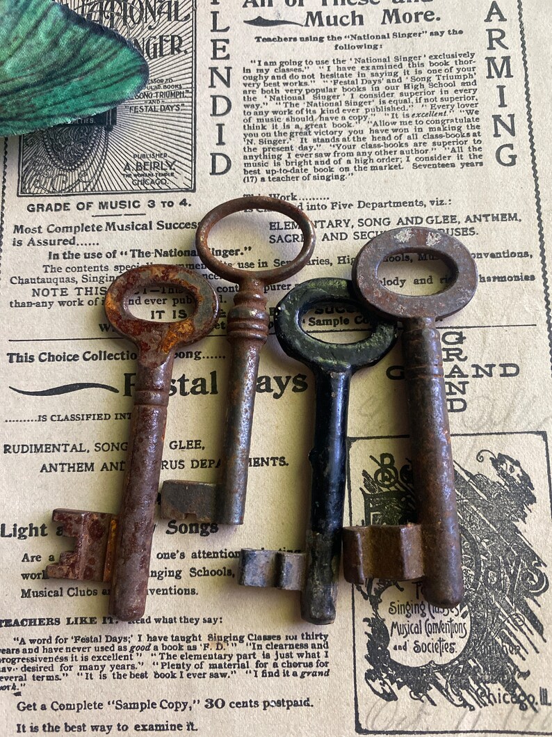 May include: Three antique keys with tarnished metal finishes. The keys are arranged on a vintage sheet of music with text about the "National Singer" and "Festal Days".