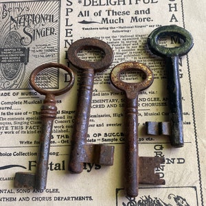 May include: Four antique keys with rusty metal finishes. The keys are arranged vertically on a vintage sheet music book with the text "Beirly's National Singer" printed on the cover. The keys are different sizes and shapes, with intricate designs and decorative elements.