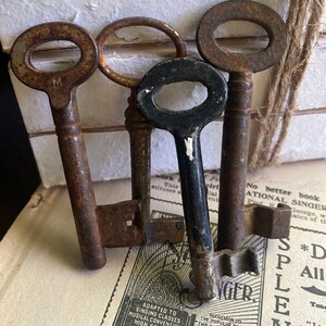 May include: Three antique keys, one black and two rusty brown, with a single keyhole on each. The keys are arranged on top of a vintage book with text about singing classes, musical conventions, high schools, and societies.