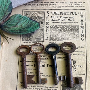 May include: Three antique keys with tarnished metal finishes. The keys are arranged on a page of a vintage music book with text about a "National Singer" and "Festal Days".