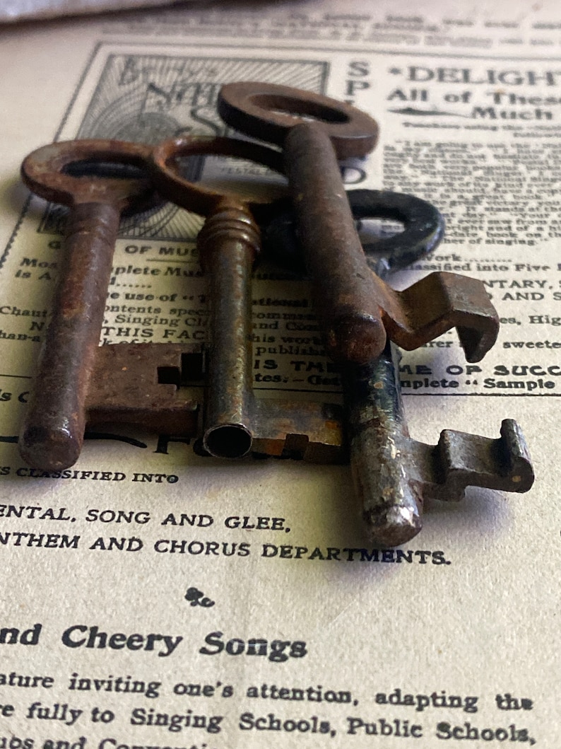 May include: Three antique keys made of metal with a worn, aged finish. The keys are arranged on top of a vintage sheet of paper with text that reads "S*DELIGHT P All of These Much".