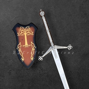 May include: A decorative sword and shield set. The sword has a silver handle and a long, silver blade. The shield is black with a brown centre and a gold tree design. The text "R Craft Creations" is visible on the shield.