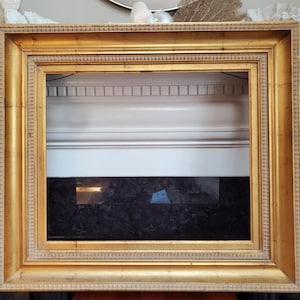 May include: A rectangular picture frame with a metallic gold finish. The frame features a wide, stepped profile with a textured, beaded inner border and a smooth, flat outer edge. The construction is solid with visible corner joints and a deep depth.