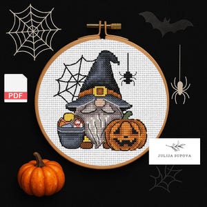 Könnte beinhalten: Ein Kreuzstich-Design mit einem Halloween-Zwerg, der einen Hexenhut trägt, einen Eimer mit Süßigkeiten hält und neben einem geschnitzten Kürbis sitzt. Das Design befindet sich in einem hölzernen Stickrahmen, mit Spinnweben und einer Fledermaus.