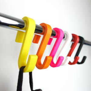 May include: A set of colourful plastic hooks hanging on a metal rod. The hooks are in the following colours: yellow, orange, pink, white, red, and black.