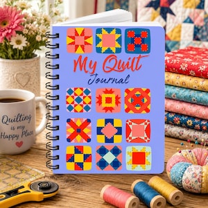 May include: A spiral-bound notebook with a light blue cover featuring colorful quilt block designs and the text "My Quilt Journal." A coffee mug with the text "Quilting is my Happy Place" sits beside the journal. Other quilting supplies are also visible.