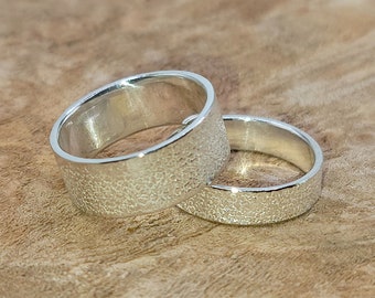 Könnte beinhalten: Zwei silberne Ringe mit einer strukturierten Oberfläche. Die Ringe liegen übereinander.