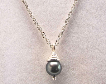 May include: A silver chain necklace with a dark gray pearl pendant. The pearl is set in a silver cap with a decorative design.